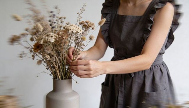 Woman arranging dried wildflower bouquet in ceramic vase, rustic neutral home decor styling