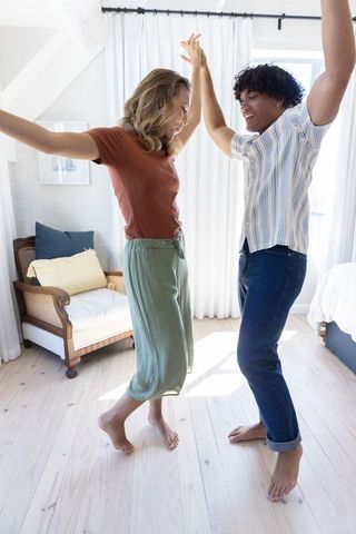 Sunlit barefoot interracial couple dancing in minimalist bedroom, joyful morning moment