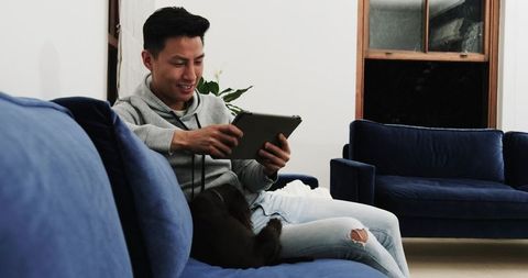 Asian man relaxing at home with tablet and dog