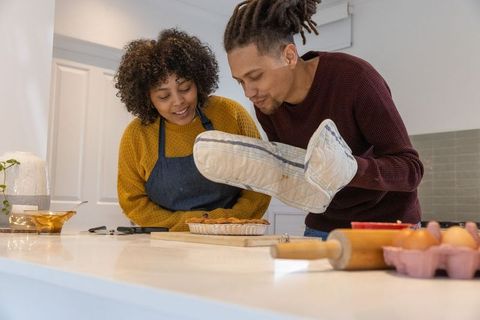 African american couple baking and checking homemade pie together in cozy modern kitchen