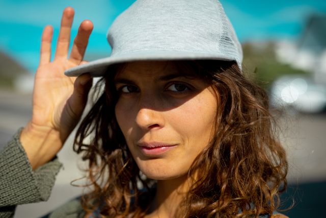 Biracial woman with curly hair wearing a baseball cap, looking confidently at the camera. Natural light enhances her features, creating a casual and active vibe. Ideal for use in lifestyle blogs, fashion articles, and advertisements promoting outdoor activities and healthy living.
