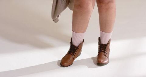 Female legs wearing brown leather ankle boots and pink socks on pale neutral studio floor