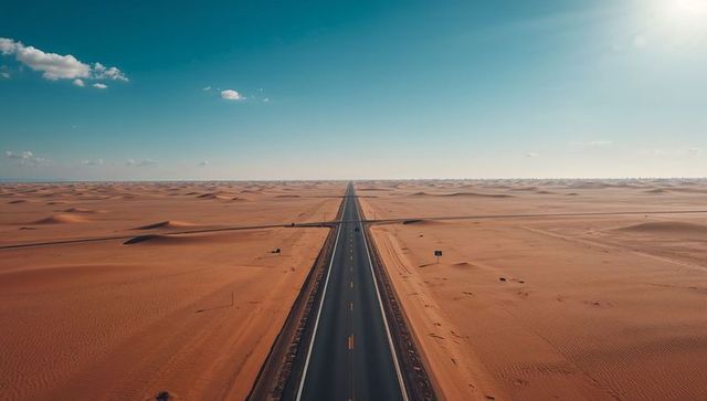 Endless desert highway stretching to horizon through vast sand dunes under clear blue sky