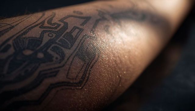 Dark skin forearm with geometric circuit tattoo in dramatic light