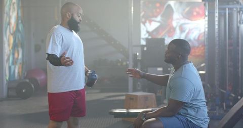 African american trainer coaching gym client holding shaker bottle, workout guidance