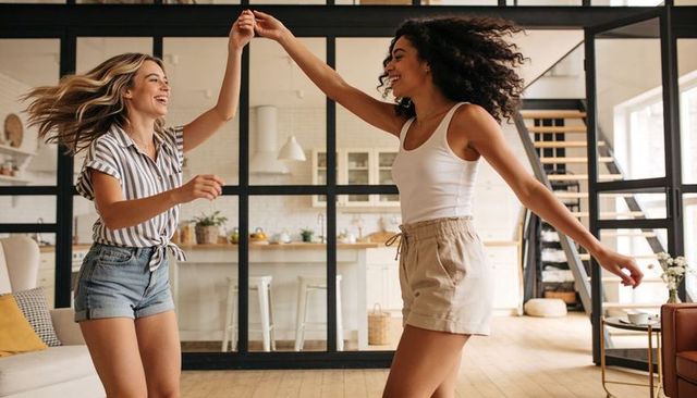 Sunlit loft friends dancing and twirling in casual summer clothes, joyful movement