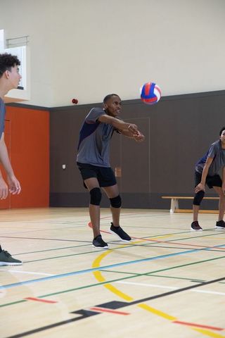 Teen volleyball team practicing forearm pass drill in indoor gymnasium training session