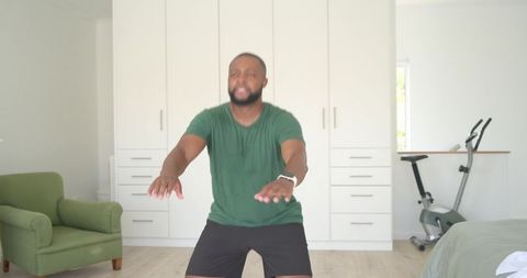 African american man performing home squats wearing smartwatch in bright minimal bedroom