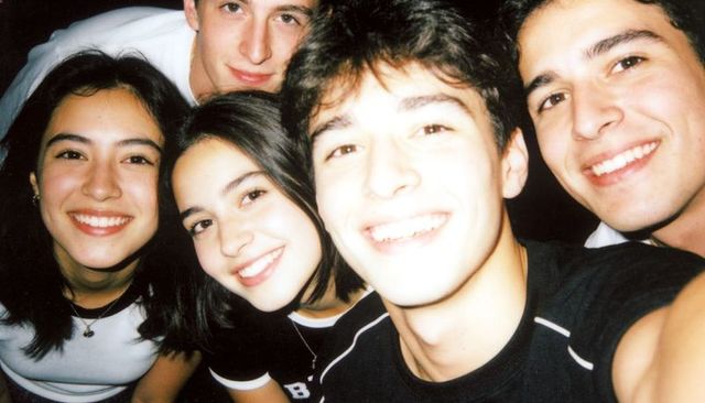 Group of five friends smiling and leaning in for nighttime selfie with flash overexposed