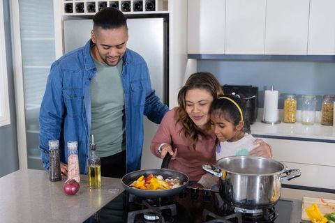 Family cooking together on modern kitchen island stirring colorful peppers and mushrooms