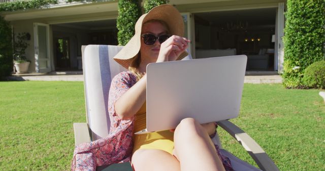 Caucasian woman using laptop while sunbathing on a deck chair in the garden. summer and working outdoor concept