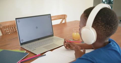 African american child wearing headphones studying remotely with laptop and notebook