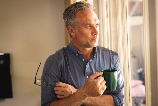 Caucasian man holding glasses and mug of coffee at window. Spending quality time at home and lifestyle concept.