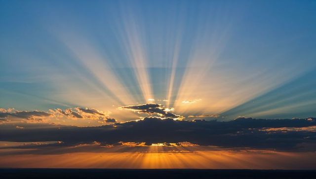 Sunburst Radiating Through Layered Clouds Casting Crepuscular Rays Over Vast Plain