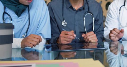 Multicultural clinical team reviewing digital patient records on tablet at glass table
