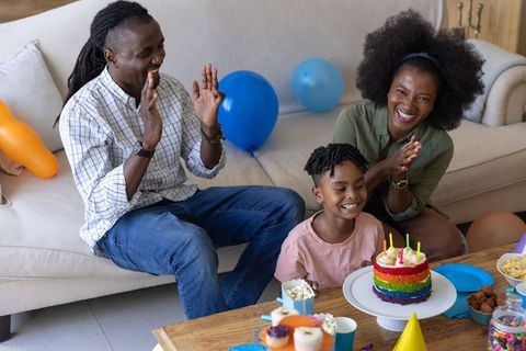 African american family celebrating child's birthday with rainbow cake and balloons