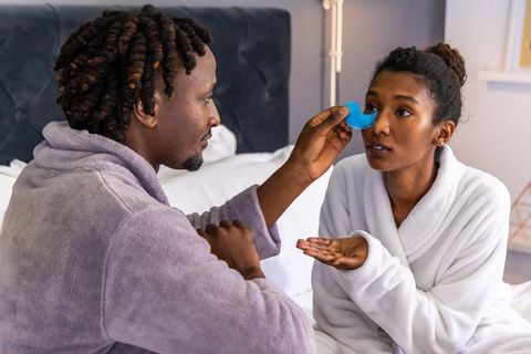 Couple practicing evening skincare routine together using eye massager in bedroom