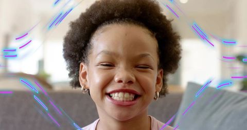 Joyful child smiling on sofa with neon streaks, playful home portrait, bright close-up