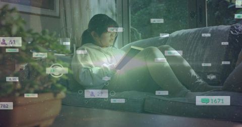 Chinese girl reading book on sunlit sofa by window while digital social ui overlays float