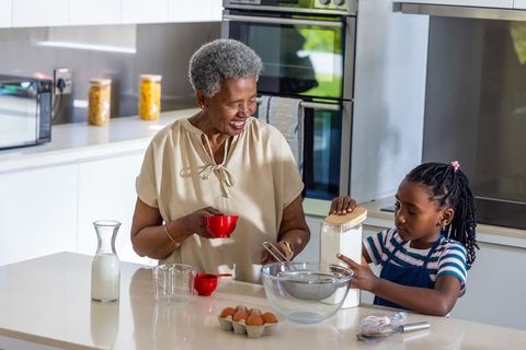 Black grandmother giving granddaughter baking lesson in bright modern kitchen