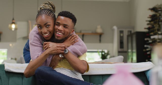 Happy African American couple hugging on a comfortable sofa at home, displaying affection and togetherness. Ideal for use in lifestyle blogs, articles on relationships, home advertisements, or social media posts about love and family.