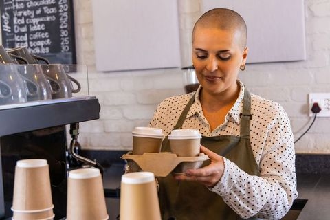 Female barista serving takeaway coffee cups in rustic brick cafe with chalkboard menu