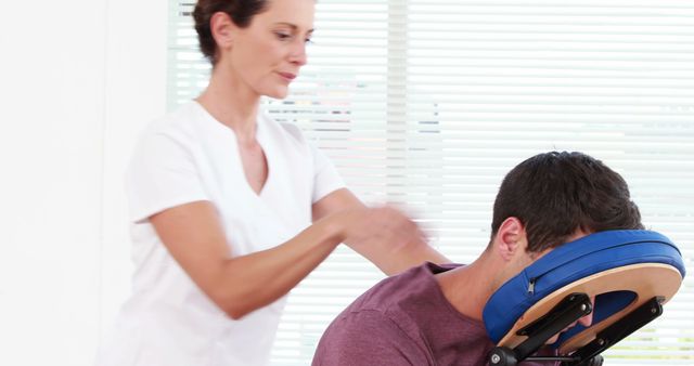 A Caucasian female massage therapist is providing a chair massage to a male client, with copy space. Chair massages like this are often used in corporate settings or events to provide quick relief from muscle tension.