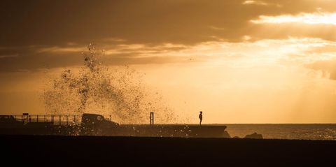 Solitary Figure by Ocean at Sunset with Dramatic Waves