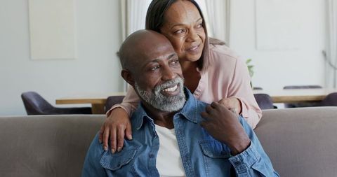 Mature diverse couple smiling on sofa sharing warm moment at home living room