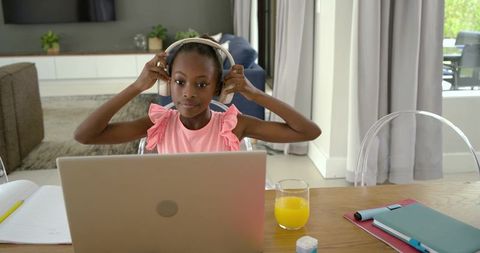 Young african girl adjusting headphones while online learning at home desk with laptop