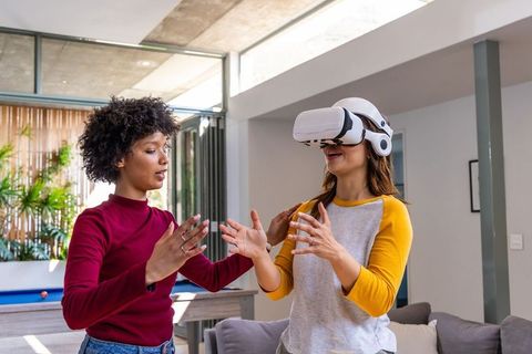 Multiracial friends guiding vr headset tester in sunlit lounge with pool table and couch