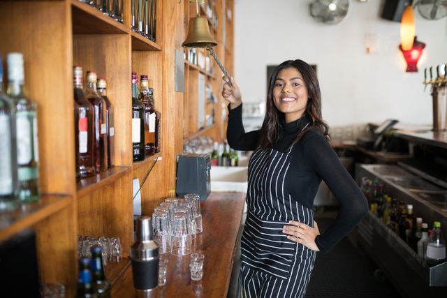 Portrait of smiling waitress ringing bell at counter in bar