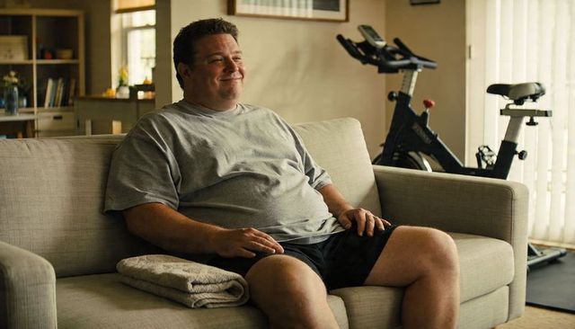 Smiling man relaxing on sofa after home workout with exercise bike in living room