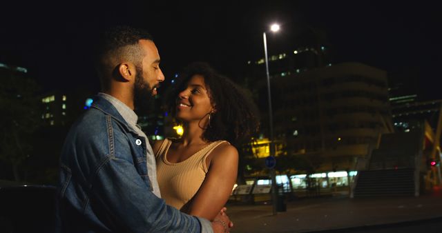 Romantic diverse couple smiling and embracing in city street at night. City living, romance, love, relationship, free time and lifestyle, unaltered.