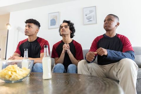 Three diverse men watching game wearing matching black and red shirts, tense anticipation