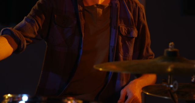 Young man enthusiastically playing drums in an oilight studio. Ideal for music-related content, illustrating live music events, concerts, or the passion and energy involved in musical practice. Suitable for blogs, websites, and advertisements focused on music education, musical instruments, or youth culture.