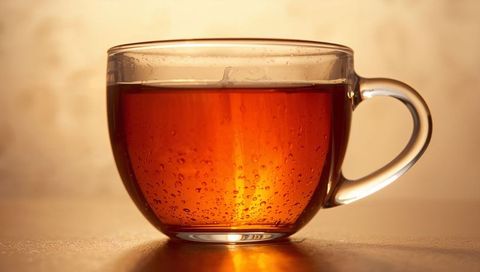 Backlit amber tea in clear glass cup with handle, condensation and warm reflections