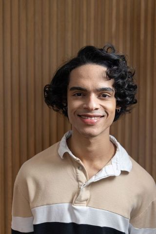 Young man smiling against wood slat wall wearing beige collared rugby shirt