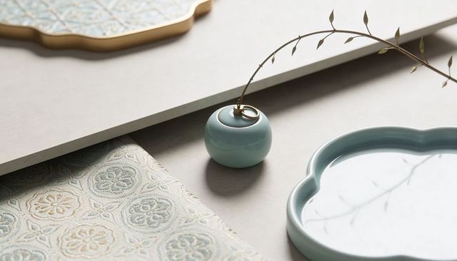 Aqua ceramic bud vase with brass collar holding dried twig beside scalloped tray pastel