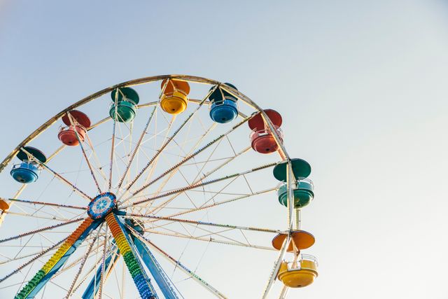Colorful Ferris wheel set against a clear sky. This represents outdoor entertainment and carnival fun. Use for themes related to amusement parks, summer activities, and events. Ideal for travel brochures, funfair promotions, and holiday advertisements.