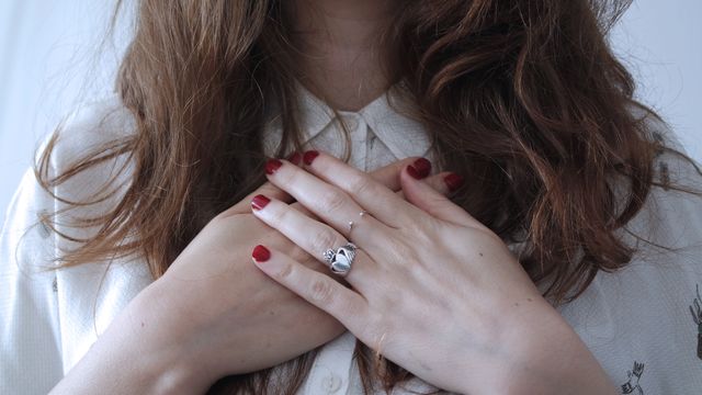 Woman places hands on her chest, displaying a silver ring with her red nails. This image can be used for themes related to gratitude, feelings, emotional moments, or for advertisements involving fashion, jewelry, and accessories.