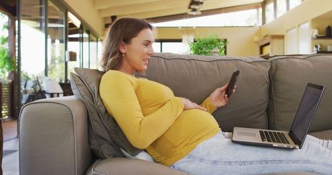 Pregnant Woman Relaxing with Smartphone and Laptop at Home