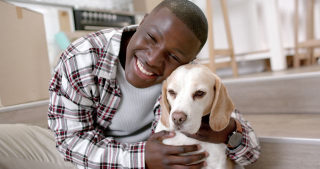 Happy african american man sitting on a floor and playing with pet dog at home. Lifestyle, pets and domestic life, unaltered.