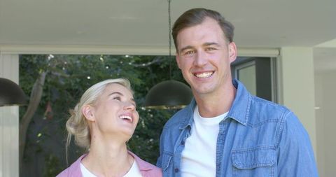Happy young couple laughing together at home with modern glass doors and garden view