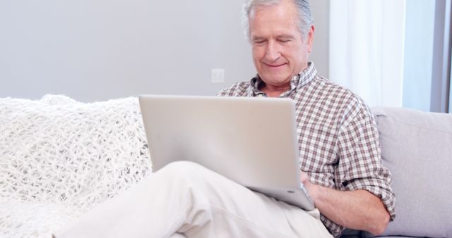 Elderly man using laptop on sofa