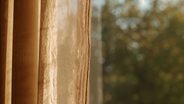 Filtering golden sunlight through sheer curtain at window, bokeh background, textured fabric