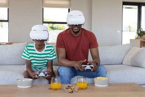 Father and Son Wearing VR Headsets Playing Video Games on Modern Living Room Couch