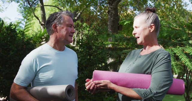 Happy senior caucasian couple talking and smiling holding yoga mats in garden. healthy retirement lifestyle.