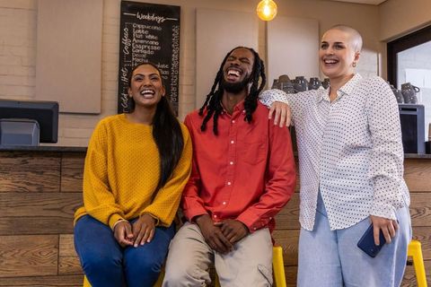 Diverse friends laughing and sitting at coffee counter on yellow stools