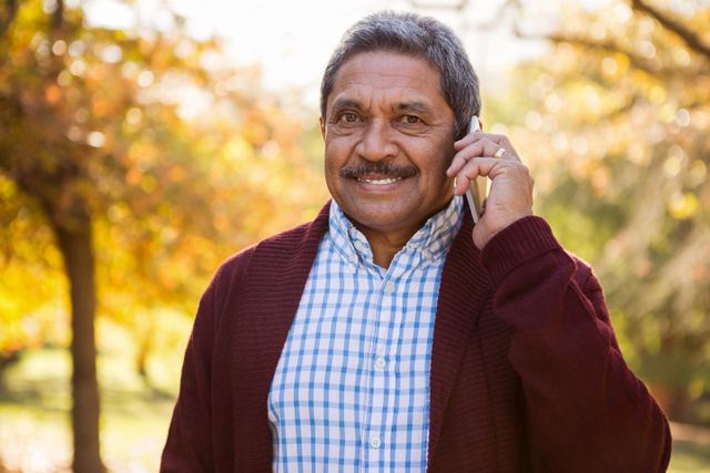 Portrait of happy mature man talking on mobile phone at park